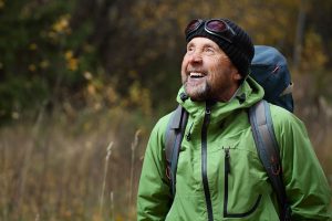 An older man smiling while hiking through a forest